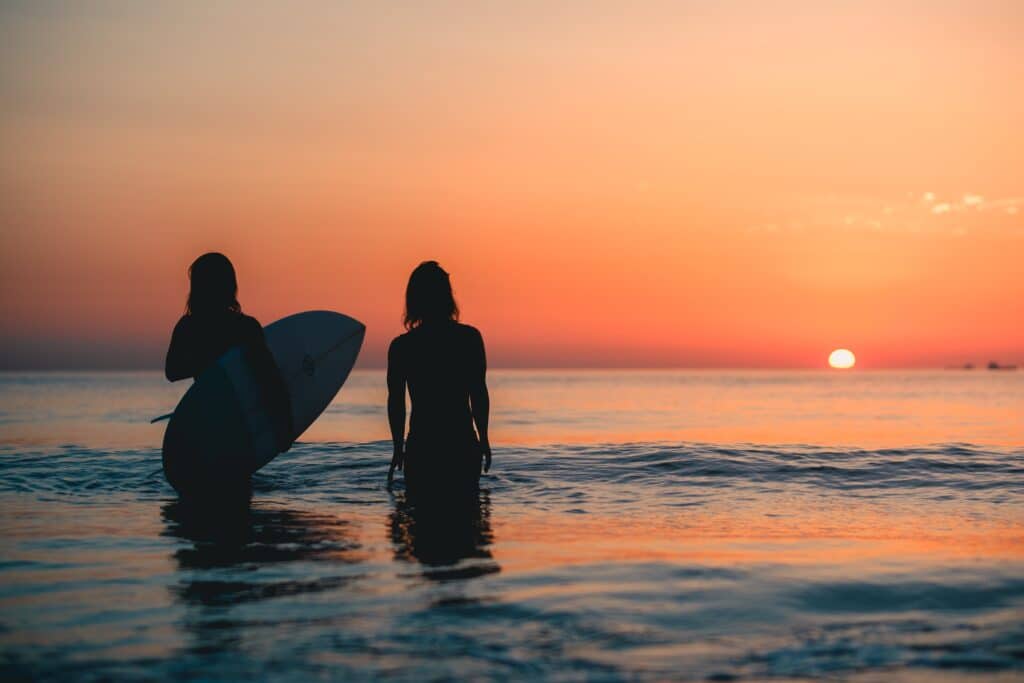 Two surfers in the sea watching the sunset.
